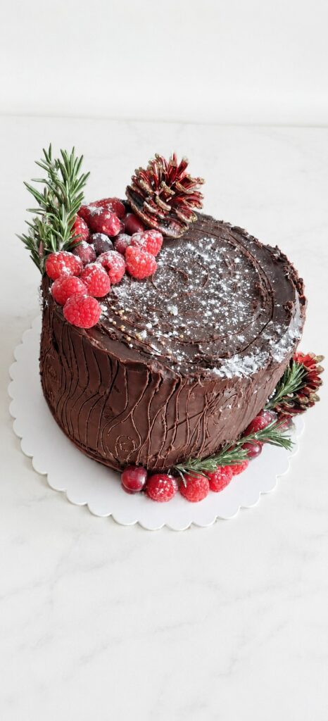 Cake design au chocolat décoré de framboises, de romarin et de pommes de pin chocolatées