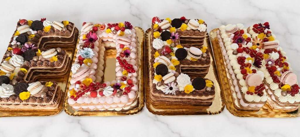 Assortiment horizontal de letter cakes décorés de fleurs et gourmandises